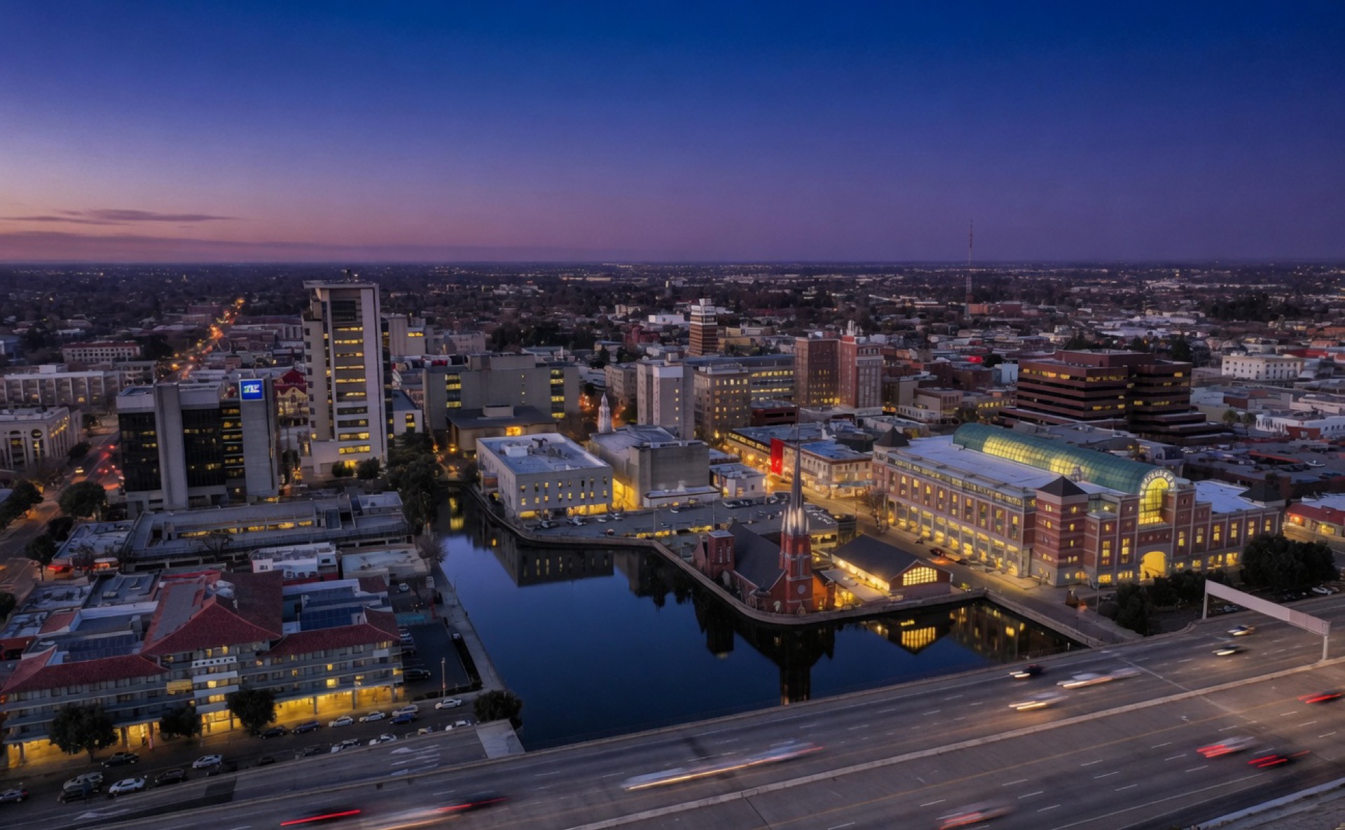 Blue-hour Stockton waterfront skyline with glowing buildings and light trails along the freeway