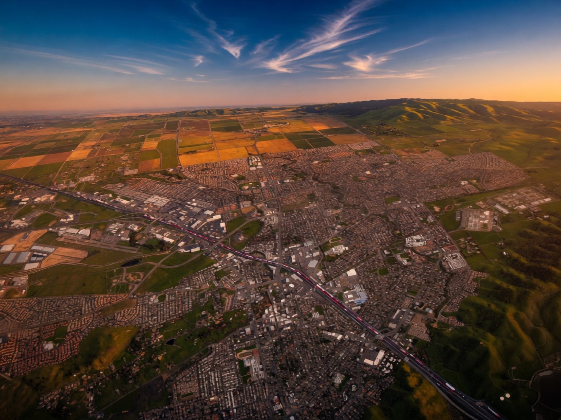 Aerial golden-hour view of Solano County city grid, agricultural fields, green hills, and the I-80 corridor